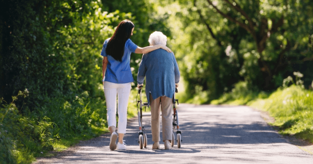 Pflegerin und lächelnde Seniorin in einem sommerlichen Garten