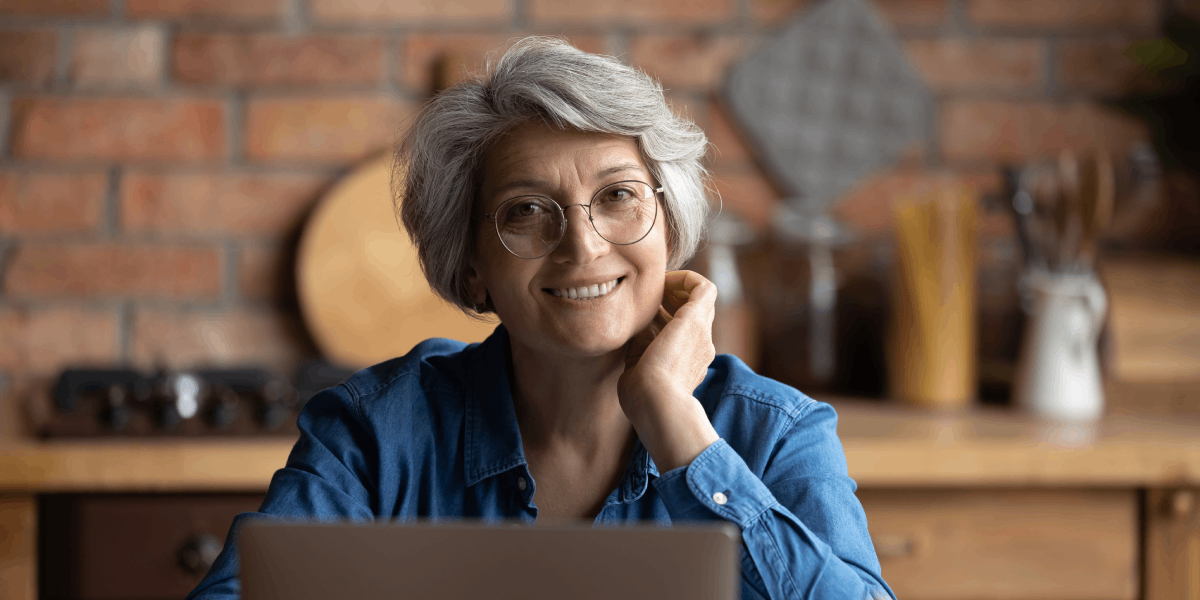 Foto: Frau sitzt am Laptop in der Küche und lächelt in die Kamera