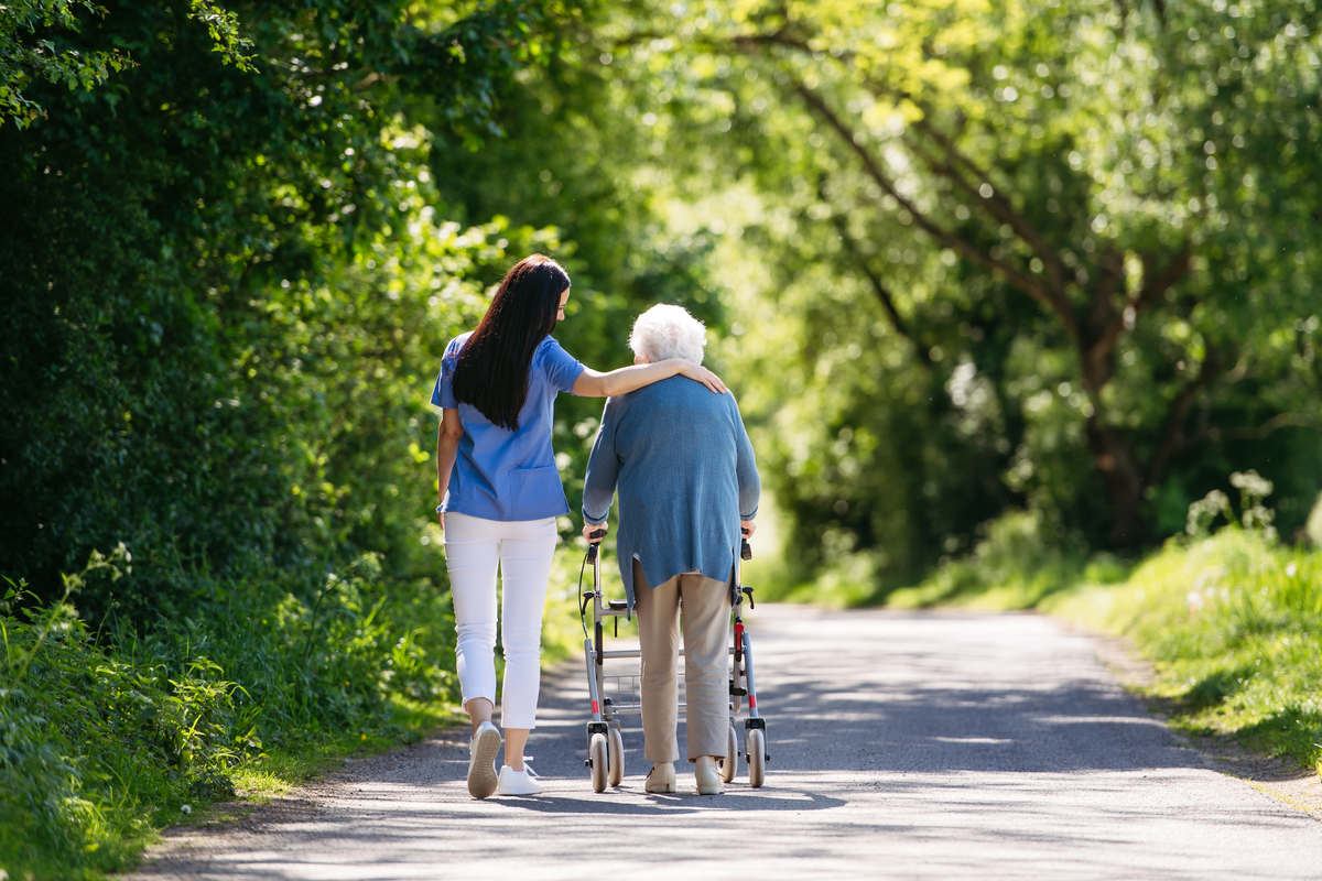 Pflegerin begleitet Seniorin mit Rollator bei einem Spaziergang