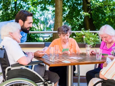 Senioren mit Betreuer sitzen auf einer Terrasse und spielen Karten
