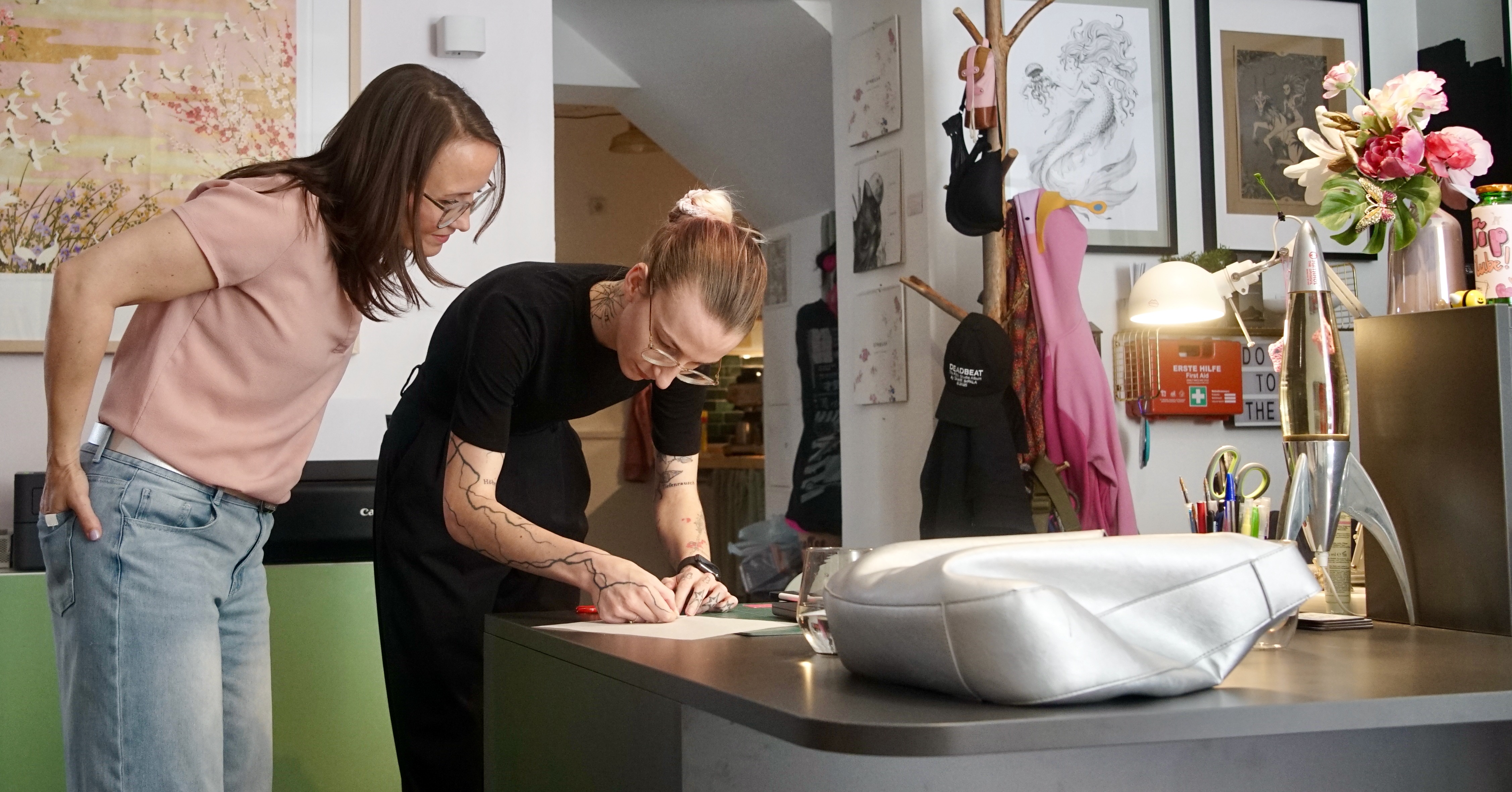 Sophie und Tätowiererin Pauline besprechen das Motiv am Empfangstresen des Ateliers