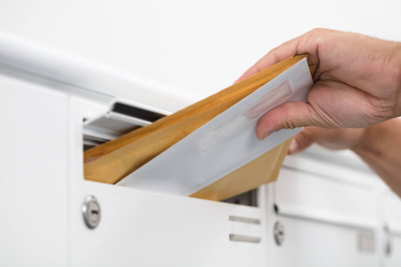Hand steckt einen Stapel Briefe in einen Briefkasten