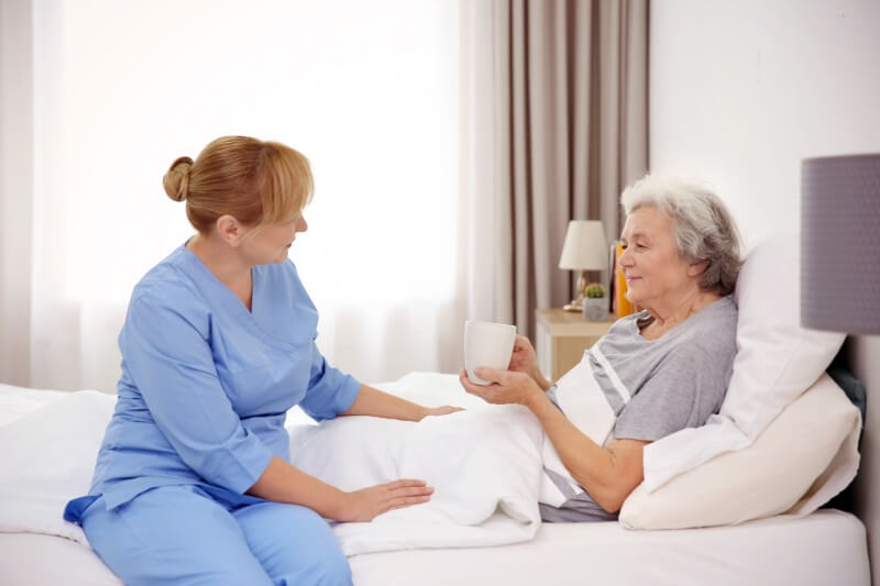 Seniorin liegt im Bett und wird von Pflegerin betreut