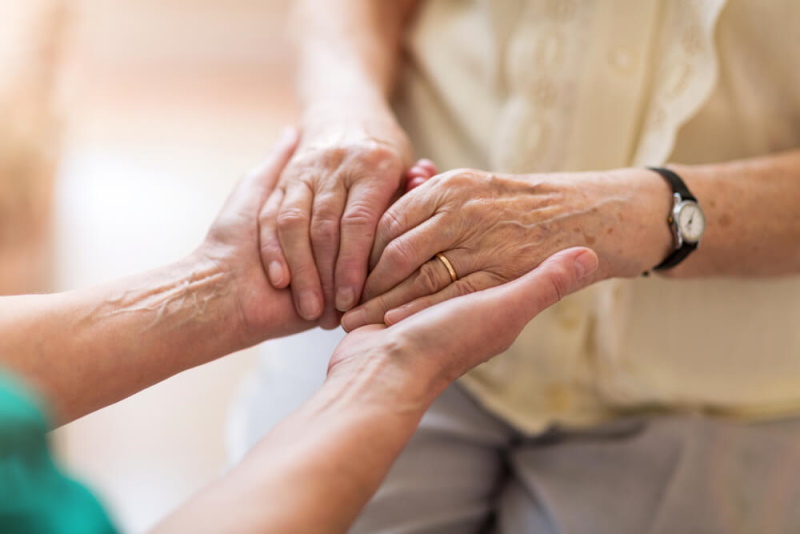 Pllegerin hält Hand von Seniorin