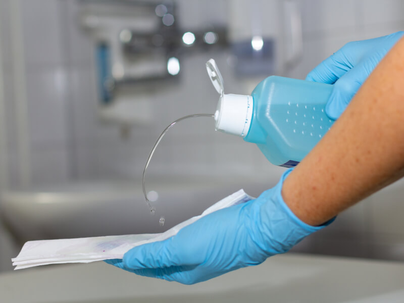 Nahaufnahme von Händen, die mit Schutzhandschuhen und Desinfektionsmittel eine Fläche reinigen