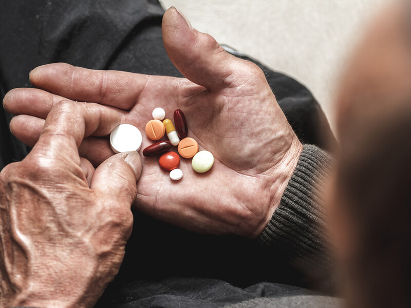 Alter Mann mit Multimorbidität hält verschiedene Medikamente in der Hand
